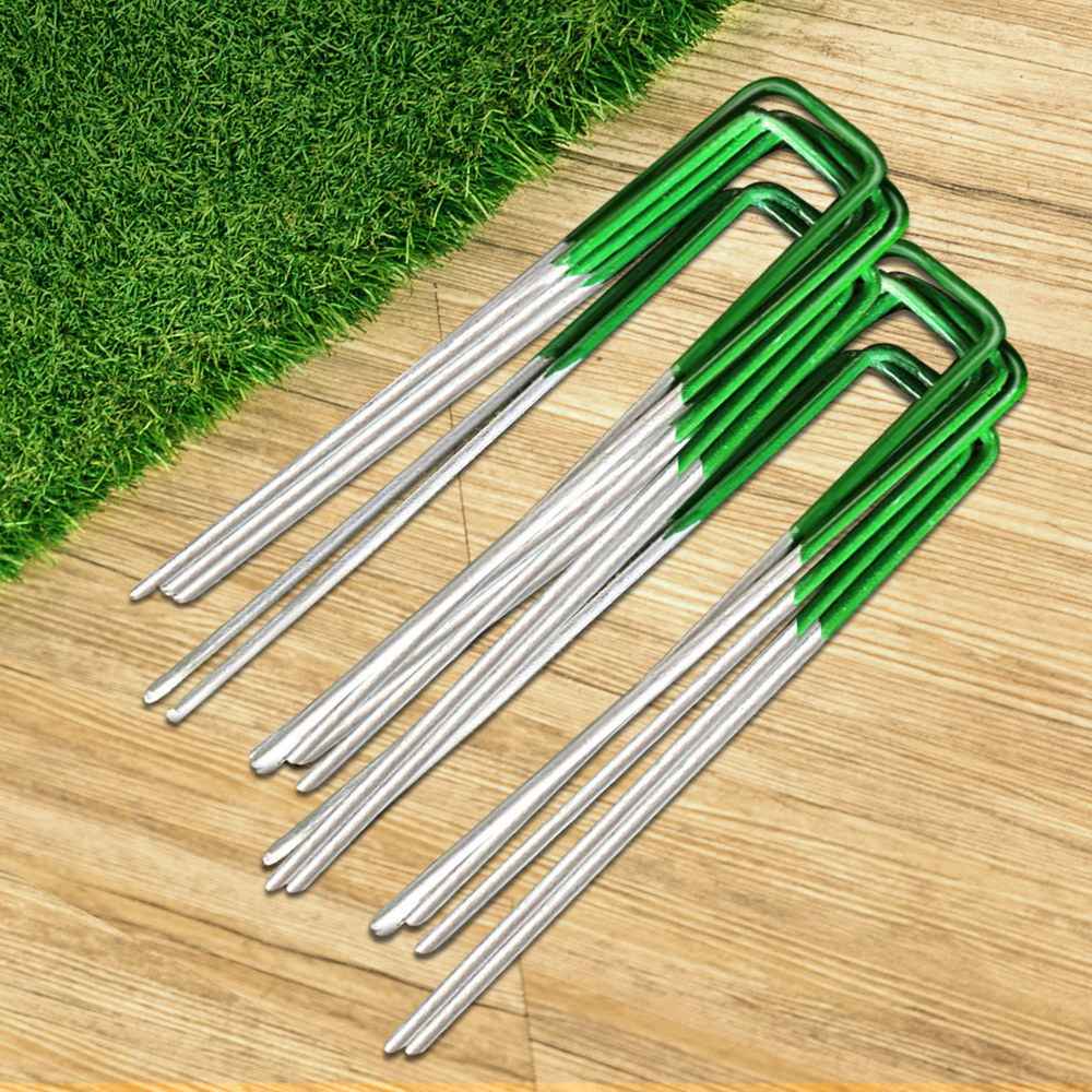 Artificial grass anchoring pins, silver spikes with green brackets, arranged on wood