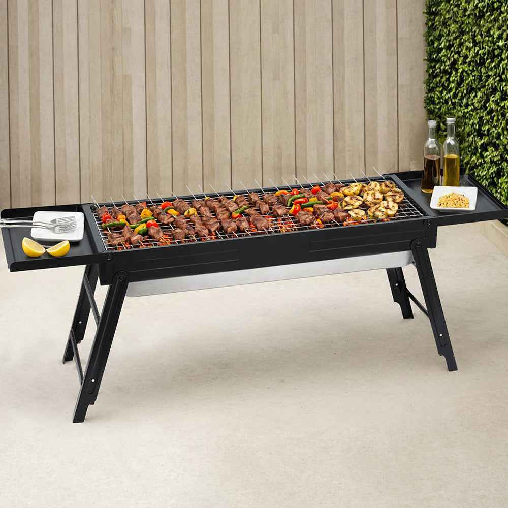 Portable charcoal BBQ grill with side shelf, black grate and folding legs on patio