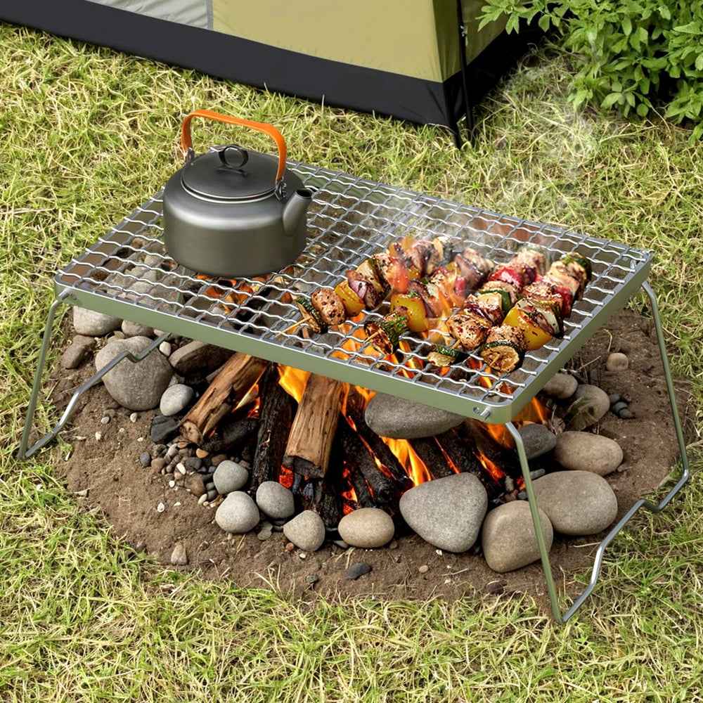 Portable charcoal grill with kettle on wire grate and grilled meat over open flames