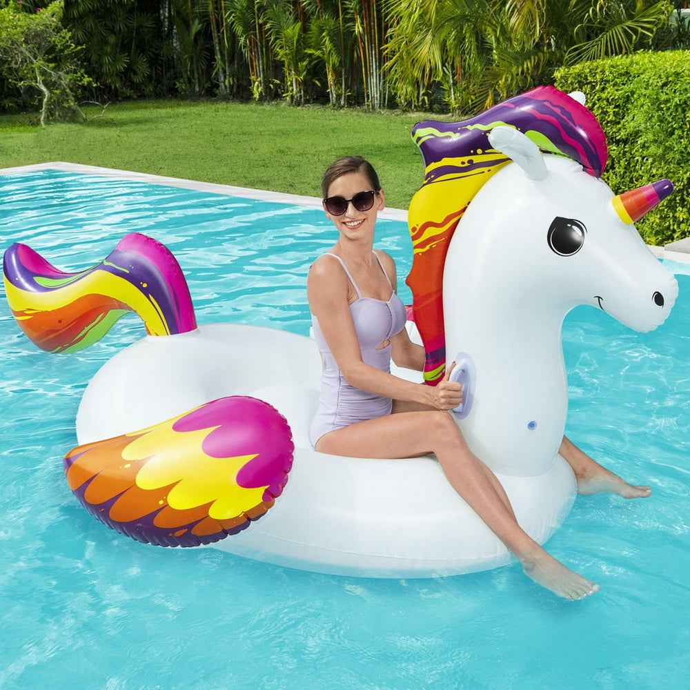 White unicorn inflatable pool rider with rainbow mane; woman relaxing on it