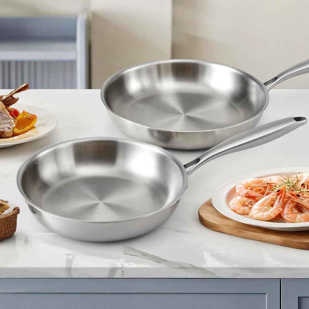 Stainless steel twin frying pans with long handles on a countertop