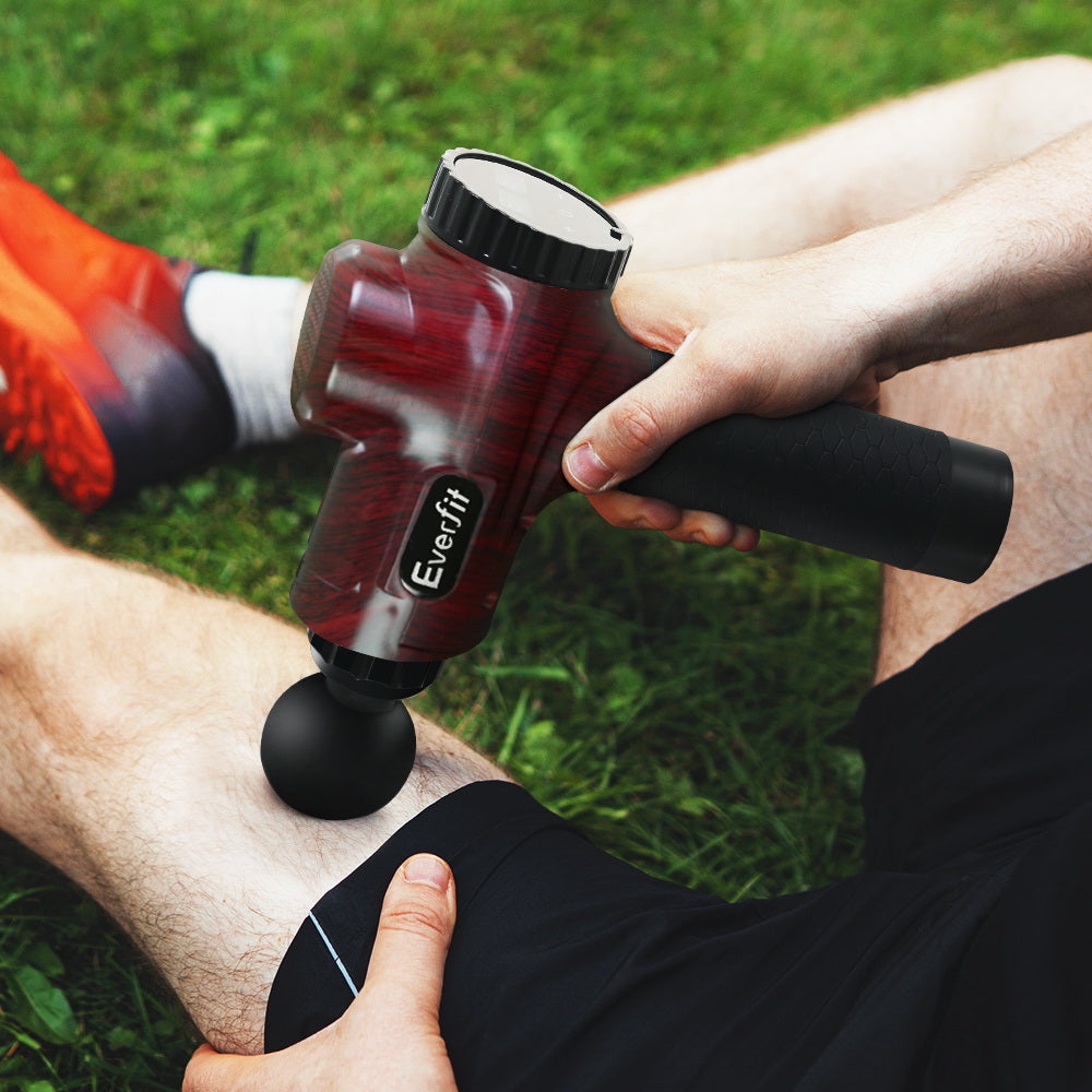 Red handheld massage gun applied to leg with black round massage head
