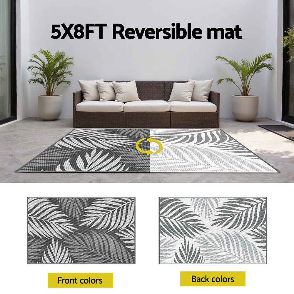 Reversible outdoor rug showing dark and light gray sides with white leaf pattern.