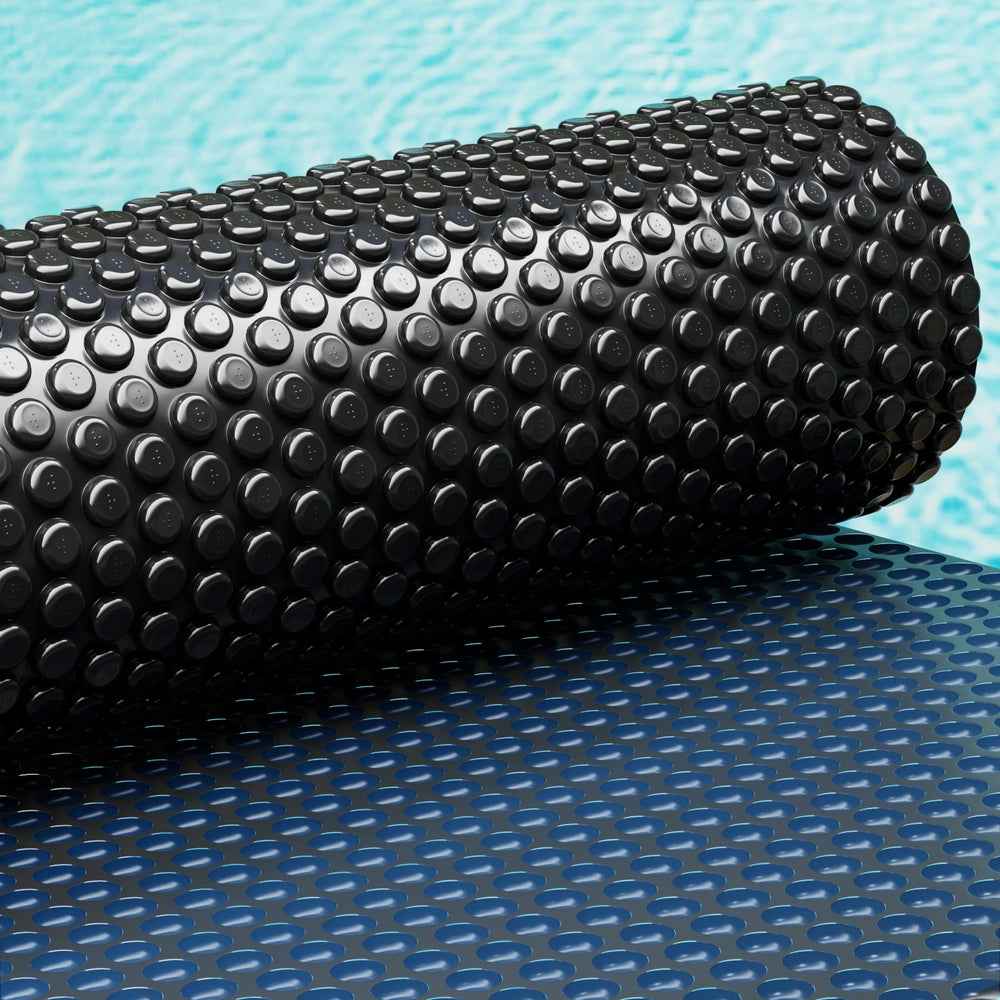 Rolled pool solar cover with black raised bubble top and blue underside bubbles
