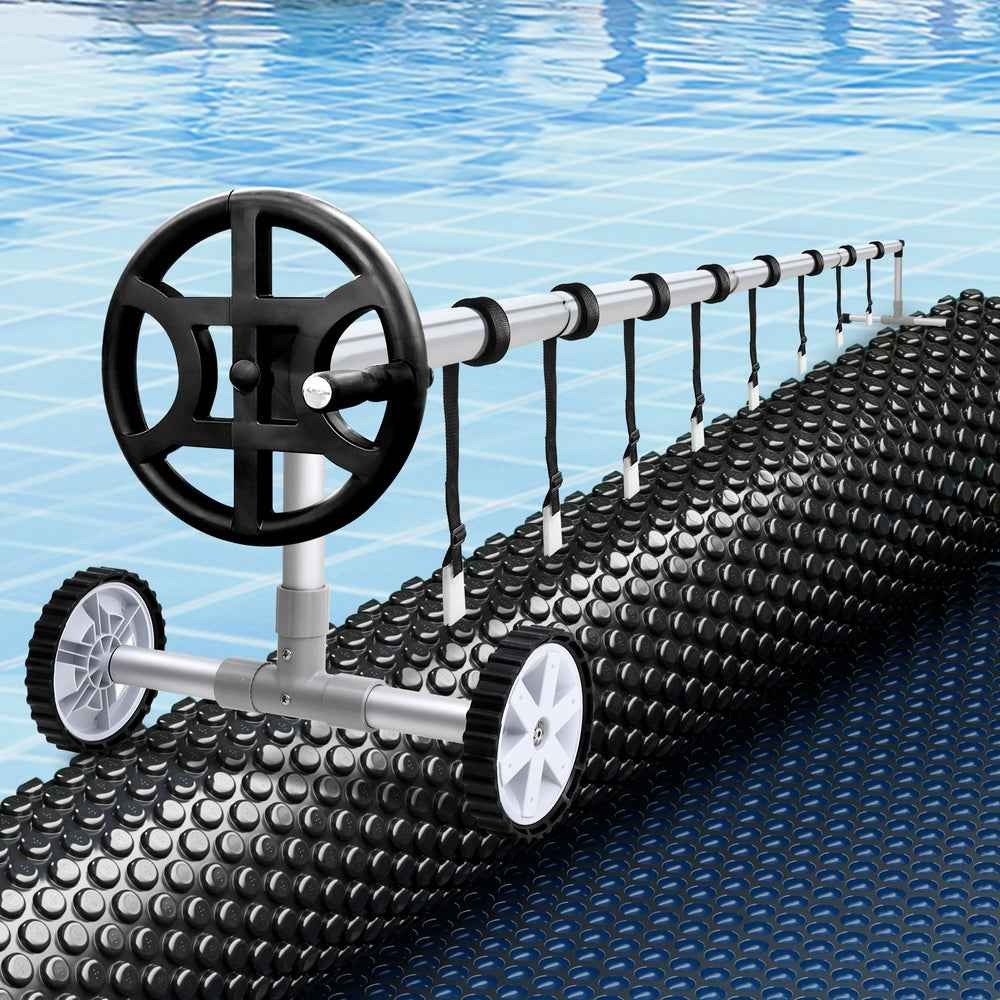 Black solar pool cover blanket on roller with large hand wheel and hanging cords