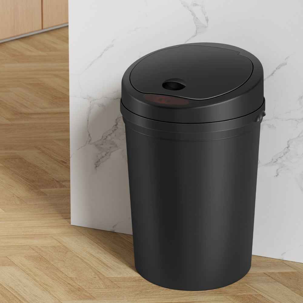 Black automatic sensor trash can standing upright with closed lid and top opening