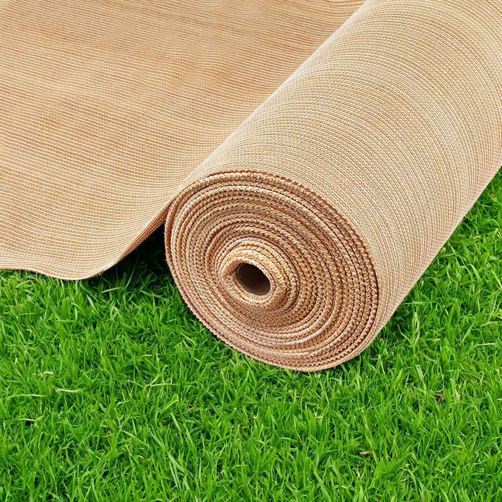 Beige shade cloth roll on green grass, tightly wound mesh weave